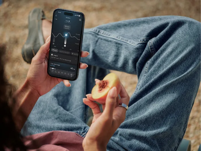 Oura Ring on a finger next to the Oura App on a smartphone