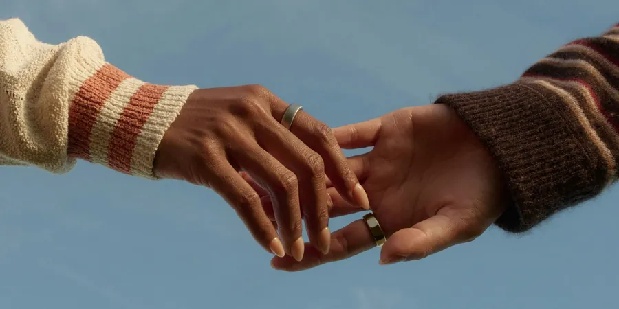 Two hands wearing Oura Ring against a blue sky