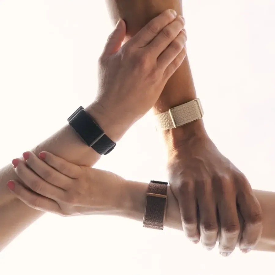 Three hands holding on to each other, each wrist wearing a Polar Loop in a different colour